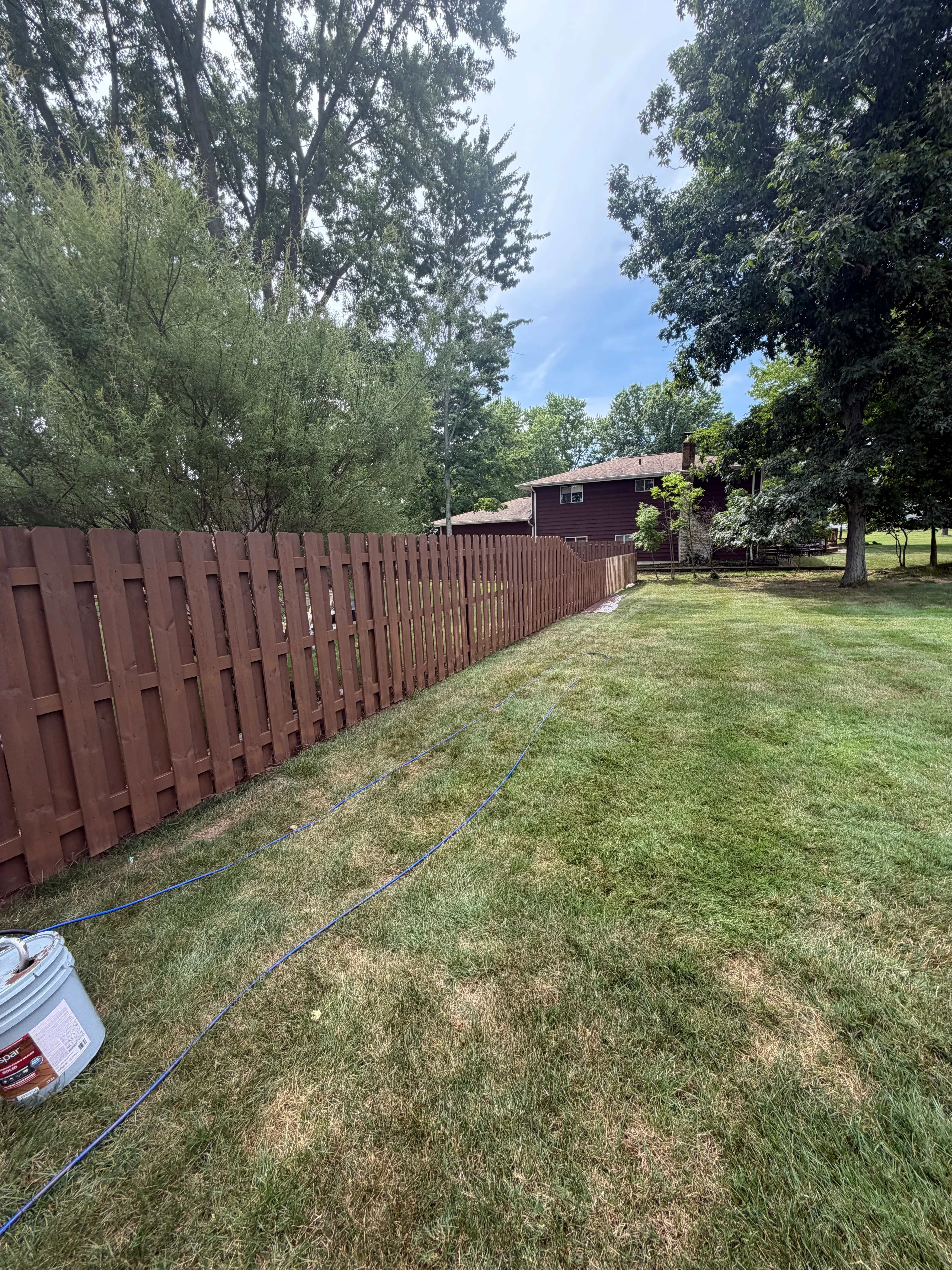 Brown-stained composite deck with blue painter's tape protecting adjacent lawn